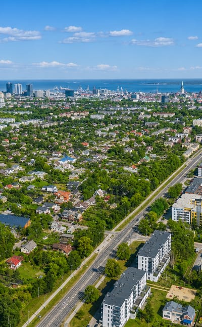 Aerial daytime view of Kristiine in Tallinn, leafy low-rise streets in front with the city centre spires, high-rises and sea beyond.