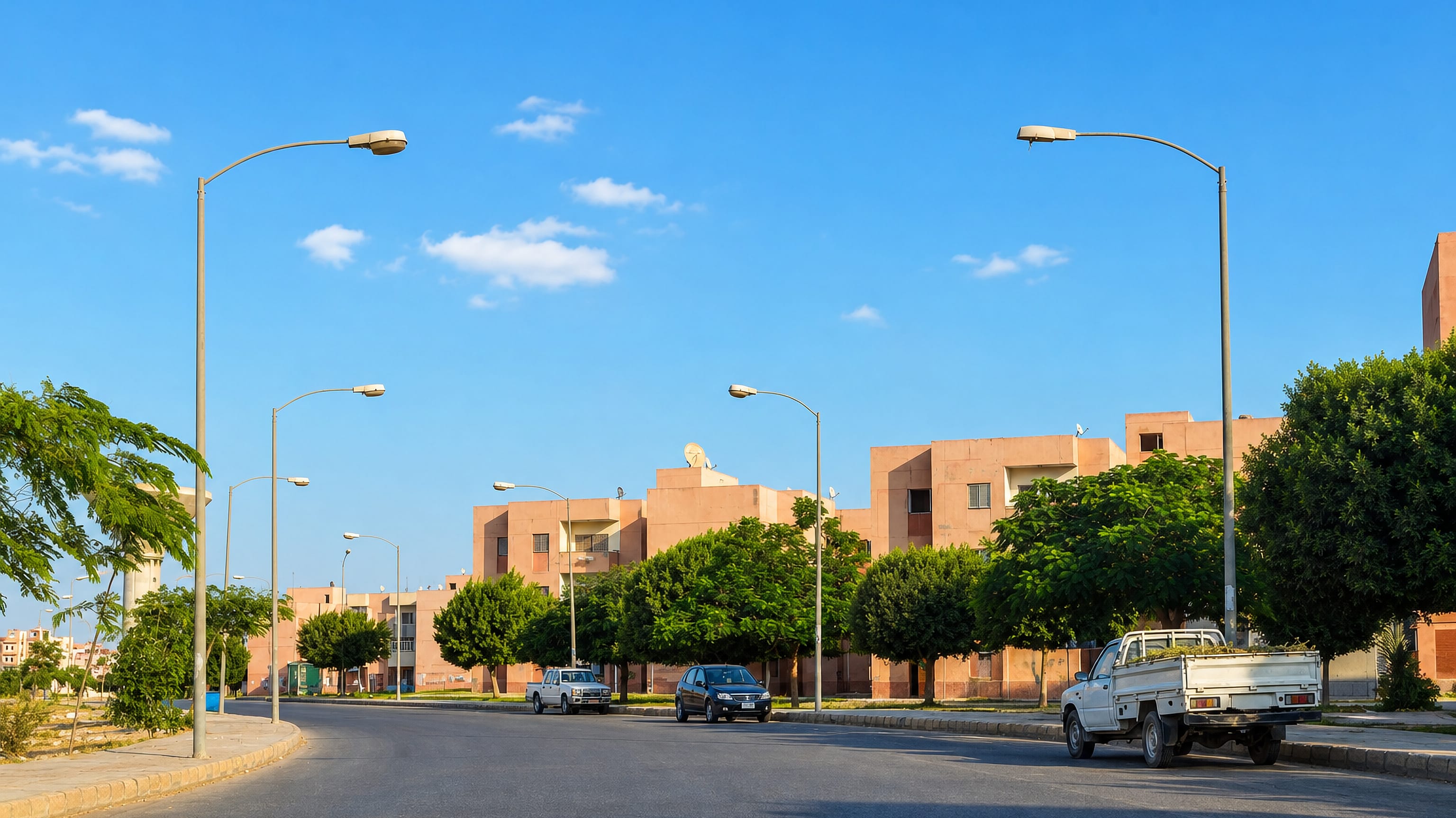 A broad tree-lined boulevard past sand-coloured apartment blocks in Madinat as Sadat, Egypt.