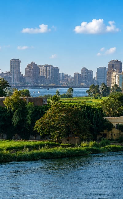Cairo skyline of mid-rise towers along the Nile River, with a minaret and a bridge crossing the water