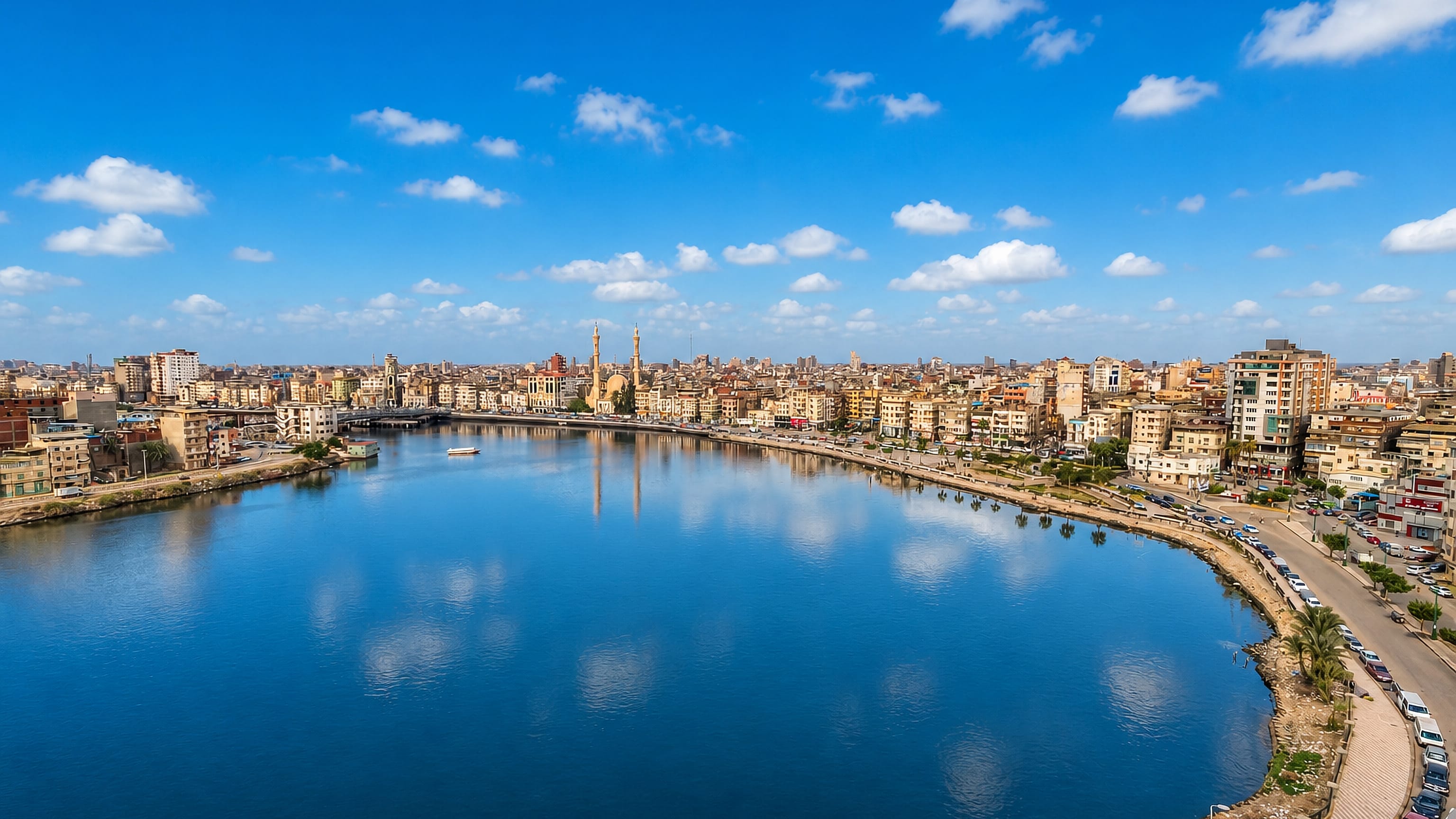 Damietta's corniche and dense riverfront buildings curving along the Nile branch, with a twin-minaret mosque.