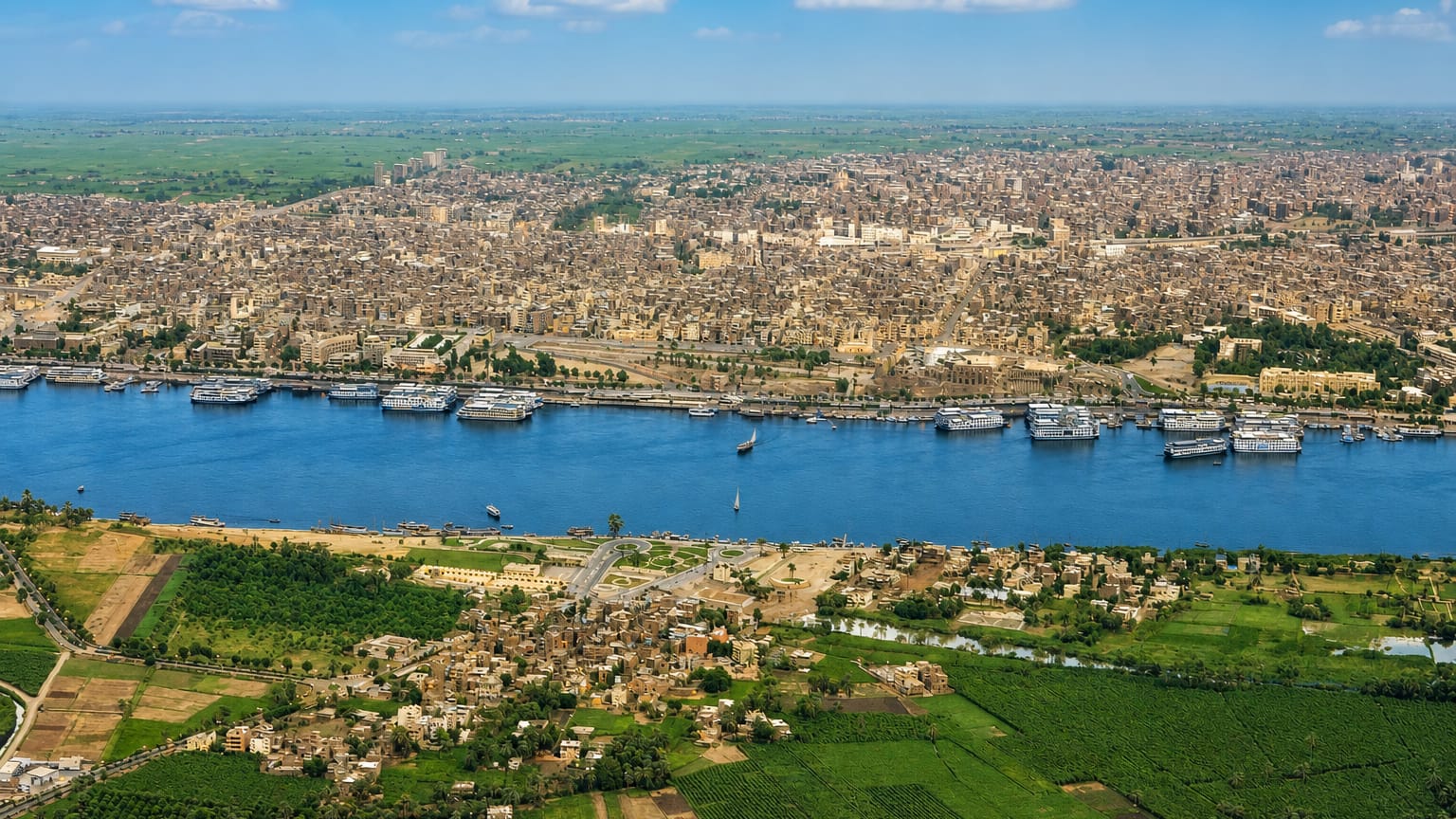 Aerial view of Luxor along the Nile with moored cruise boats and green West Bank fields