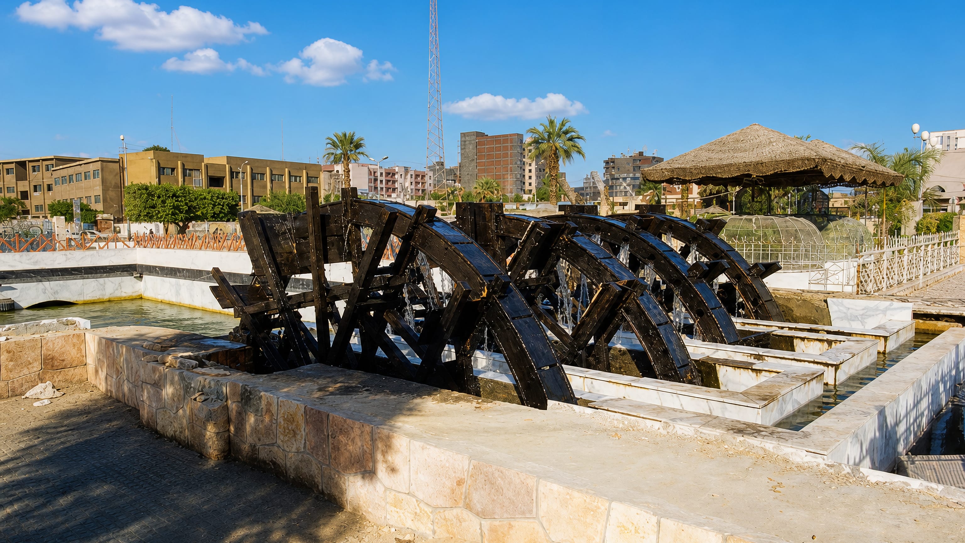 Wooden waterwheels turning in the canal at Al Fayyum, Egypt, with the town's low-rise buildings behind.
