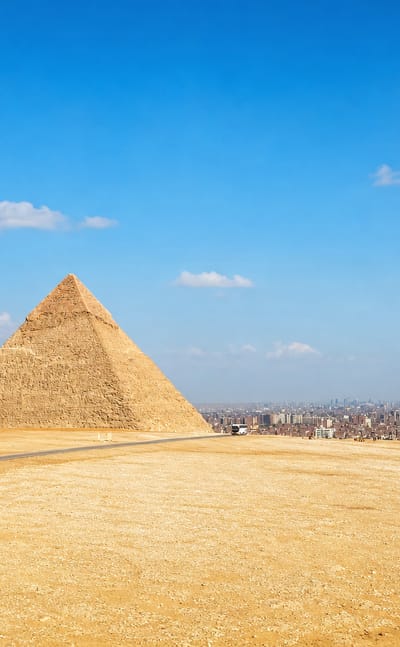 The three Pyramids of Giza on the desert plateau with Cairo's skyline stretching behind.