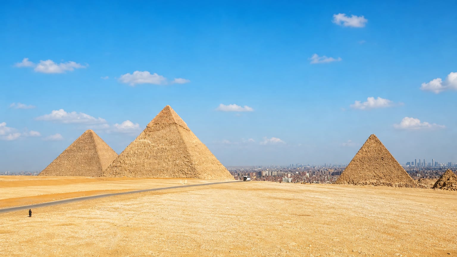 The three Pyramids of Giza on the desert plateau with Cairo's skyline stretching behind.