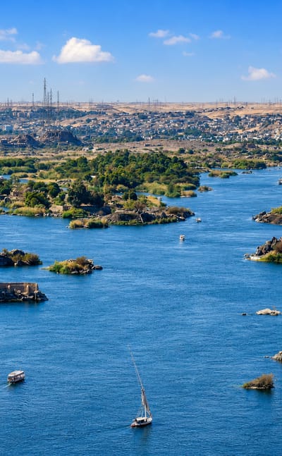 The Nile winding past granite islands and desert dunes at Aswan, with feluccas under sail.