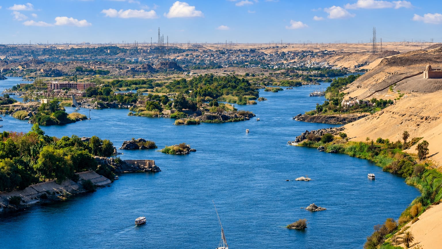 The Nile winding past granite islands and desert dunes at Aswan, with feluccas under sail.