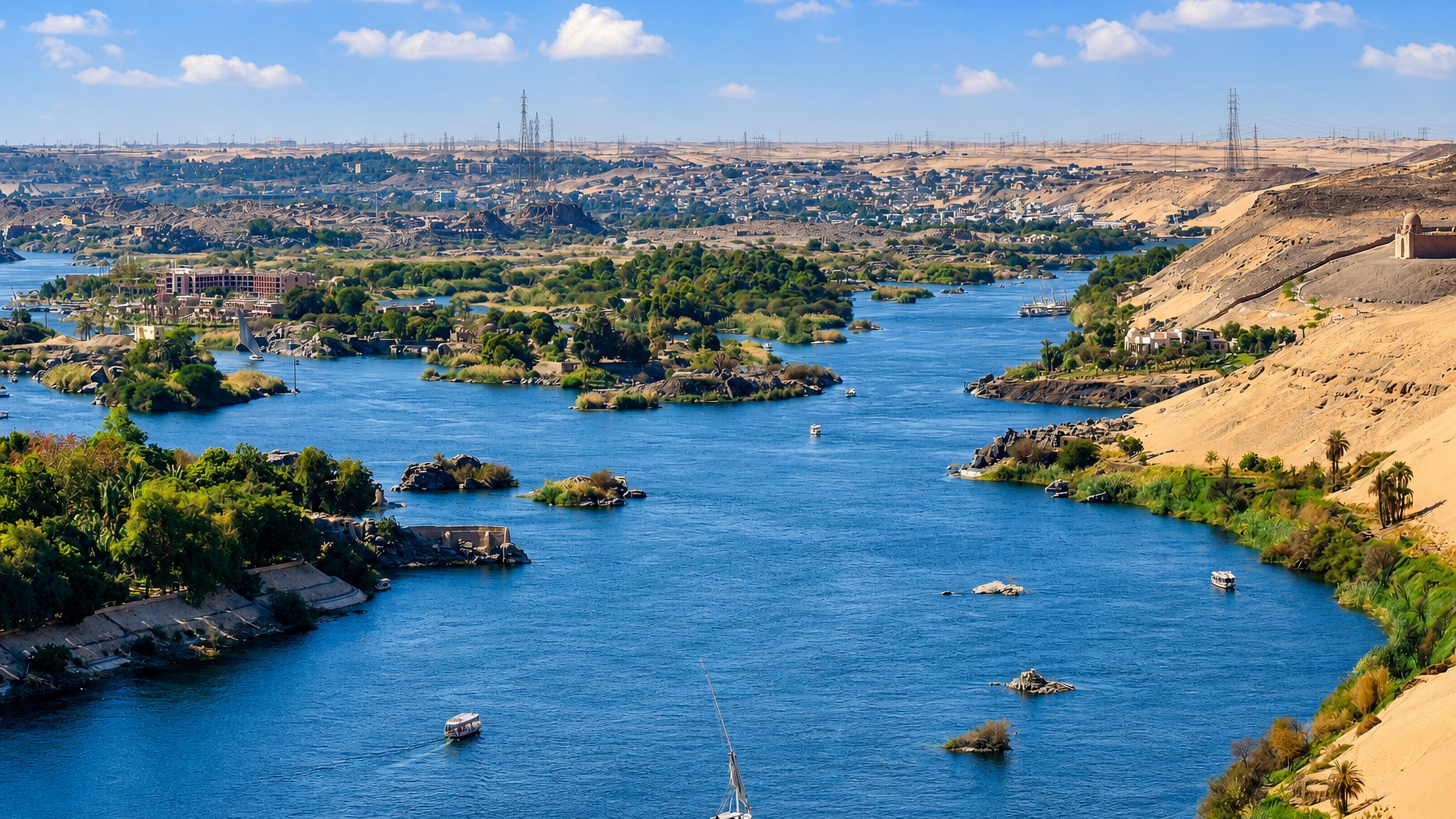The Nile winding past granite islands and desert dunes at Aswan, with feluccas under sail.