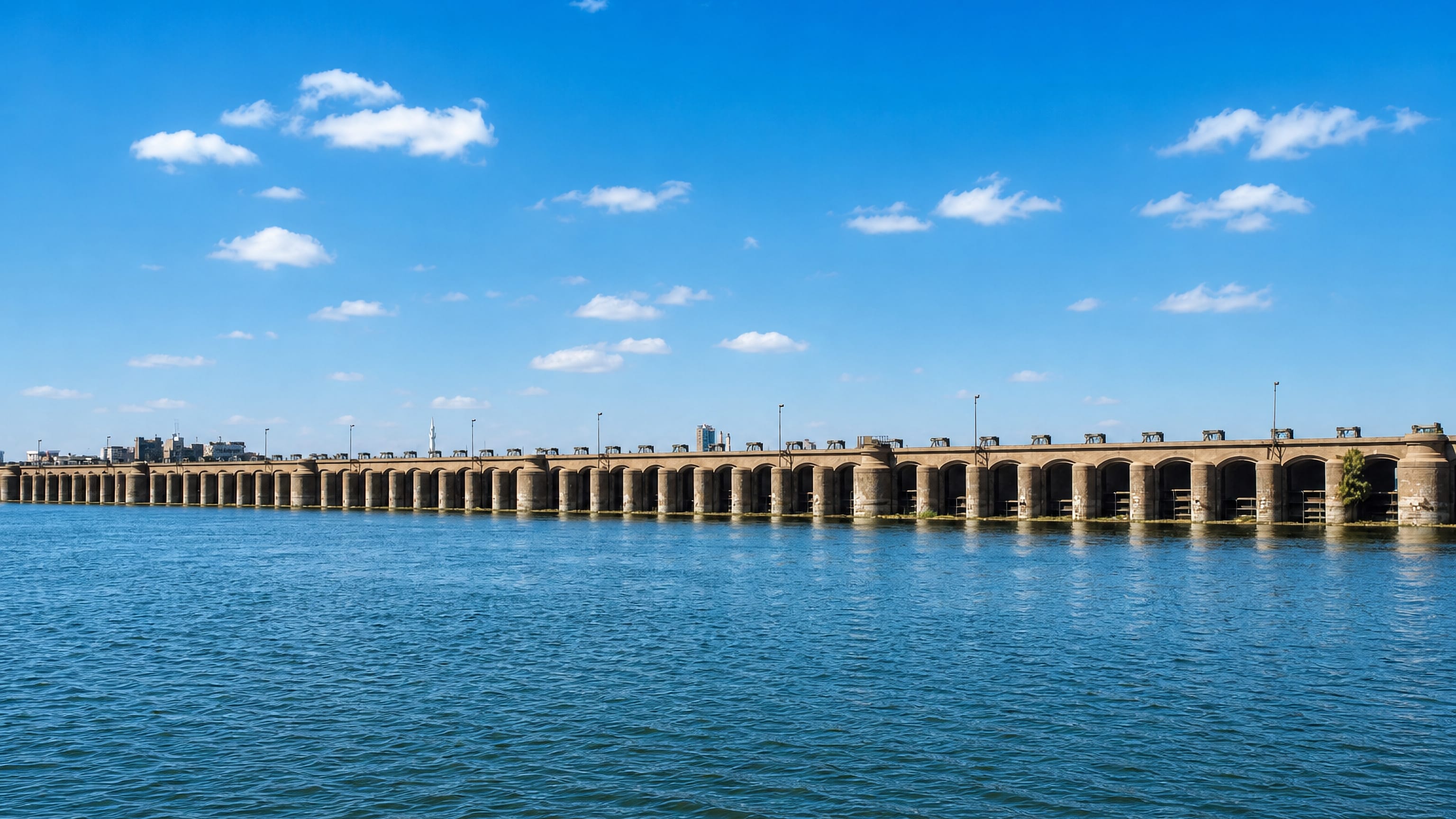 The long arched Assiut Barrage spanning the Nile, with the Egyptian city's skyline on the far bank.