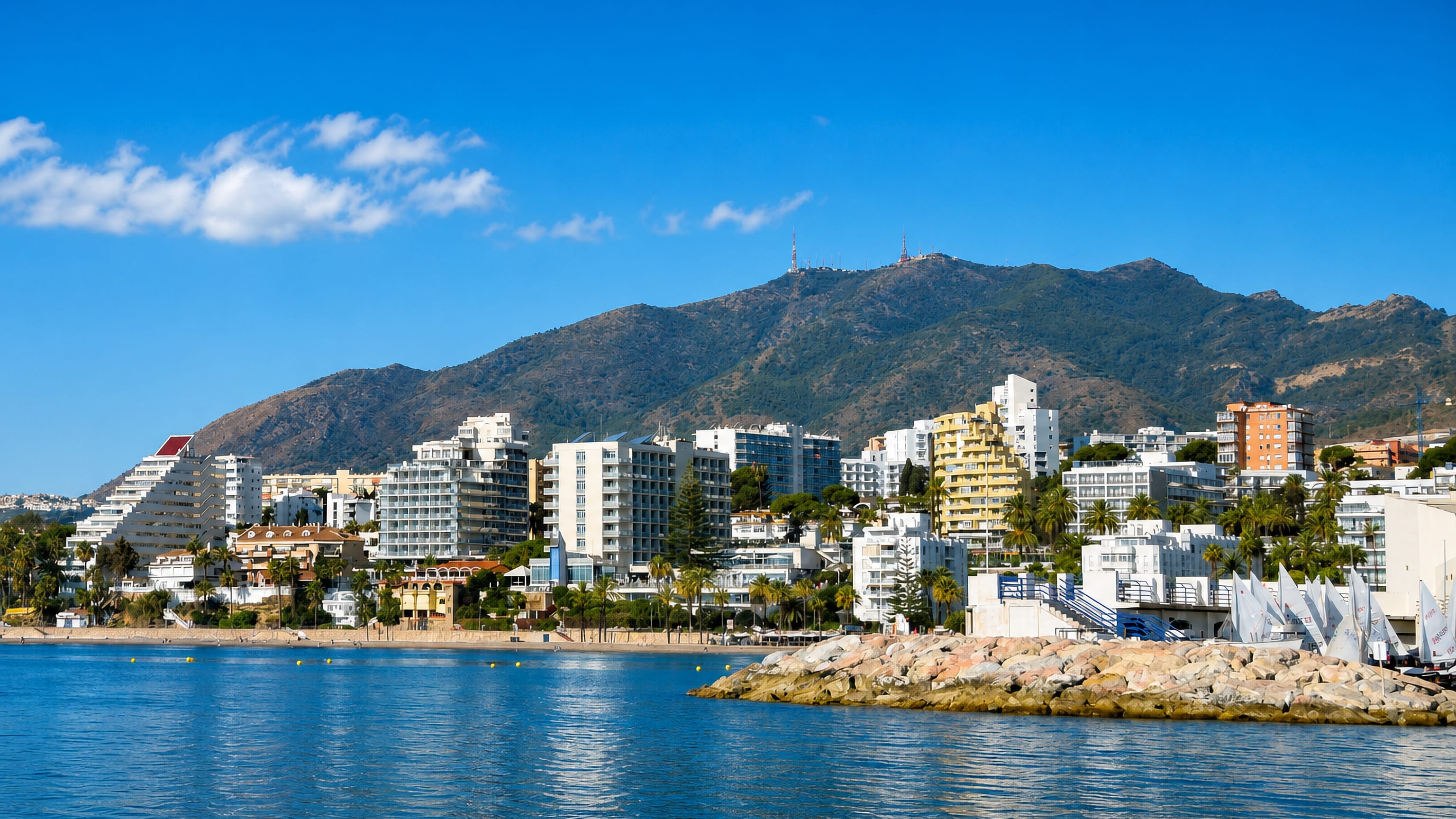 Benalmádena's white seafront apartment blocks and palms rising beneath a mountain ridge above the Mediterranean.