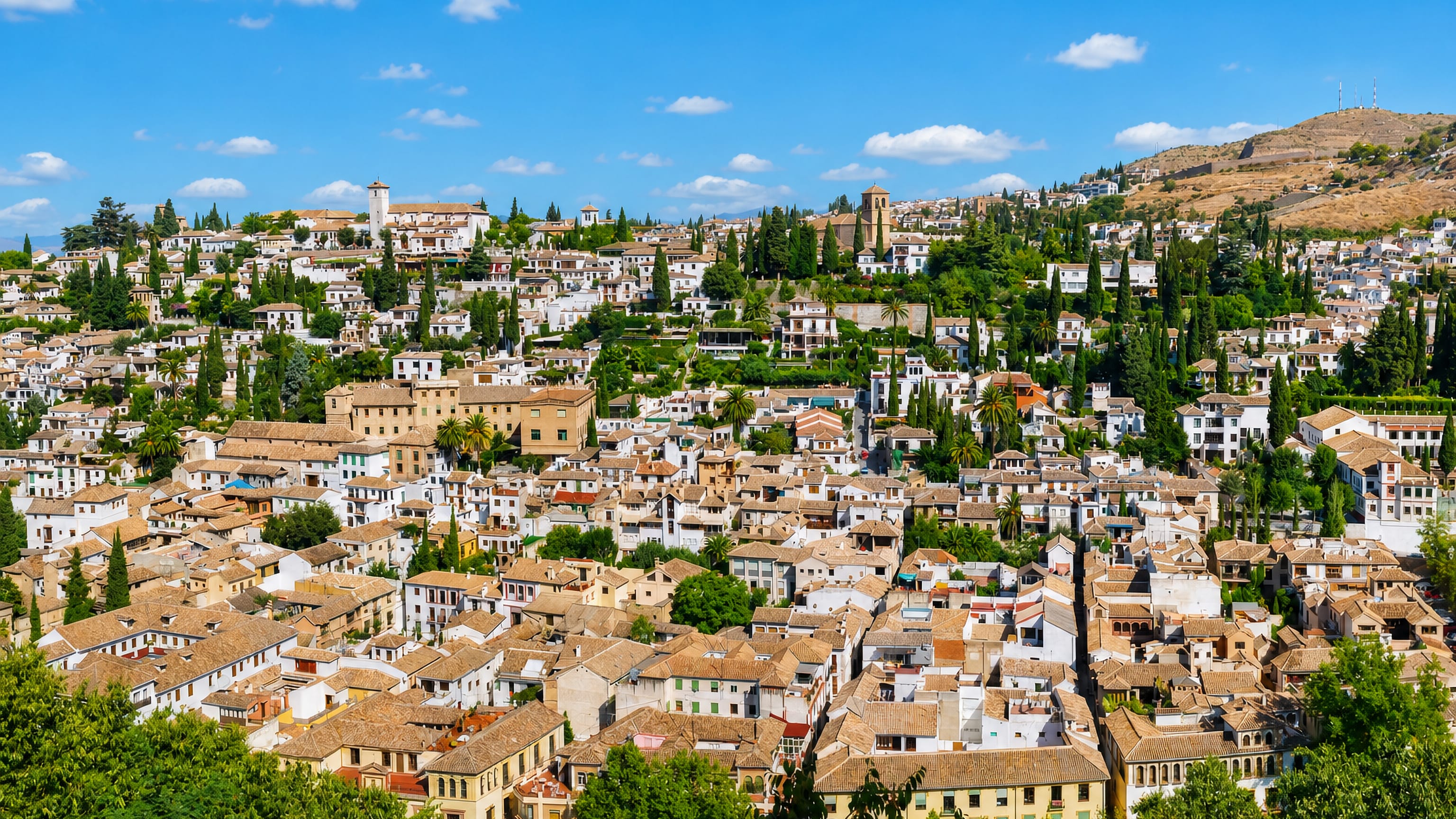 Whitewashed houses and terracotta roofs of the Albaicín quarter climbing the hillside in Granada, Spain.