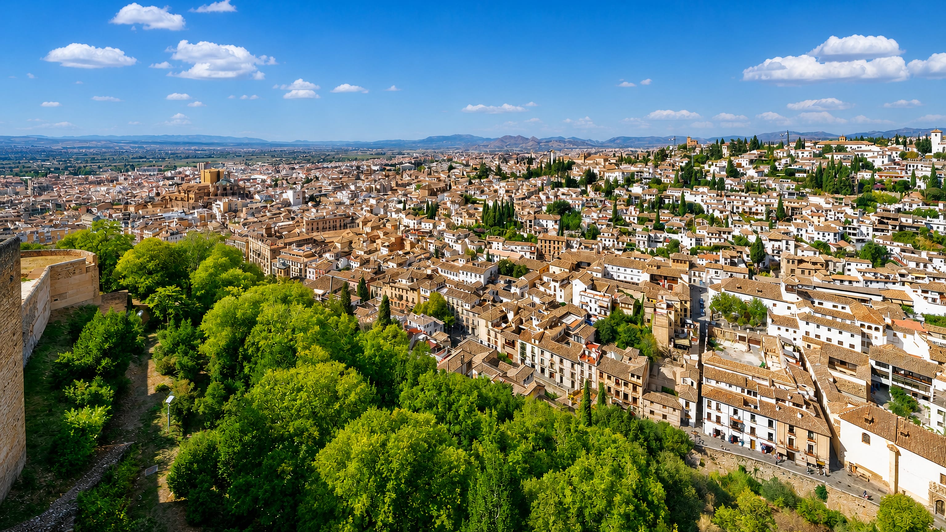 Granada's Albaicín quarter of whitewashed houses seen from the Alhambra ramparts, with the cathedral and sierra beyond