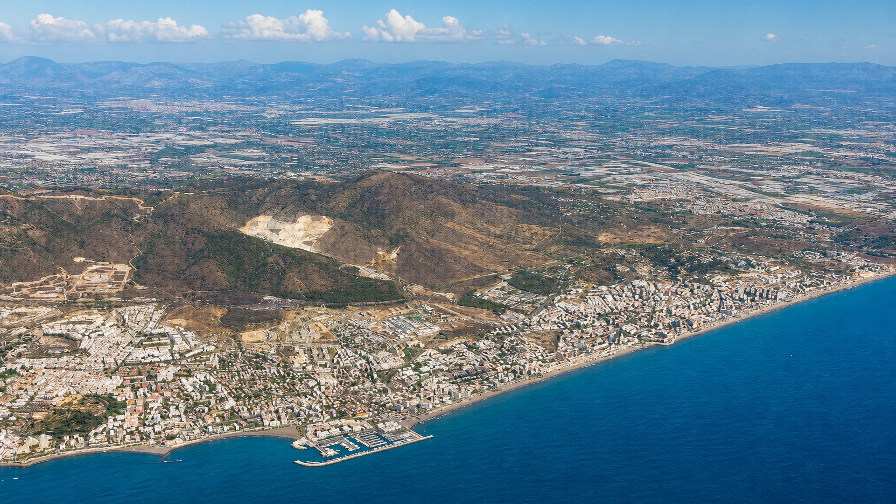 Torremolinos and the Costa del Sol coastline from the air, with beach, marina and inland hills.