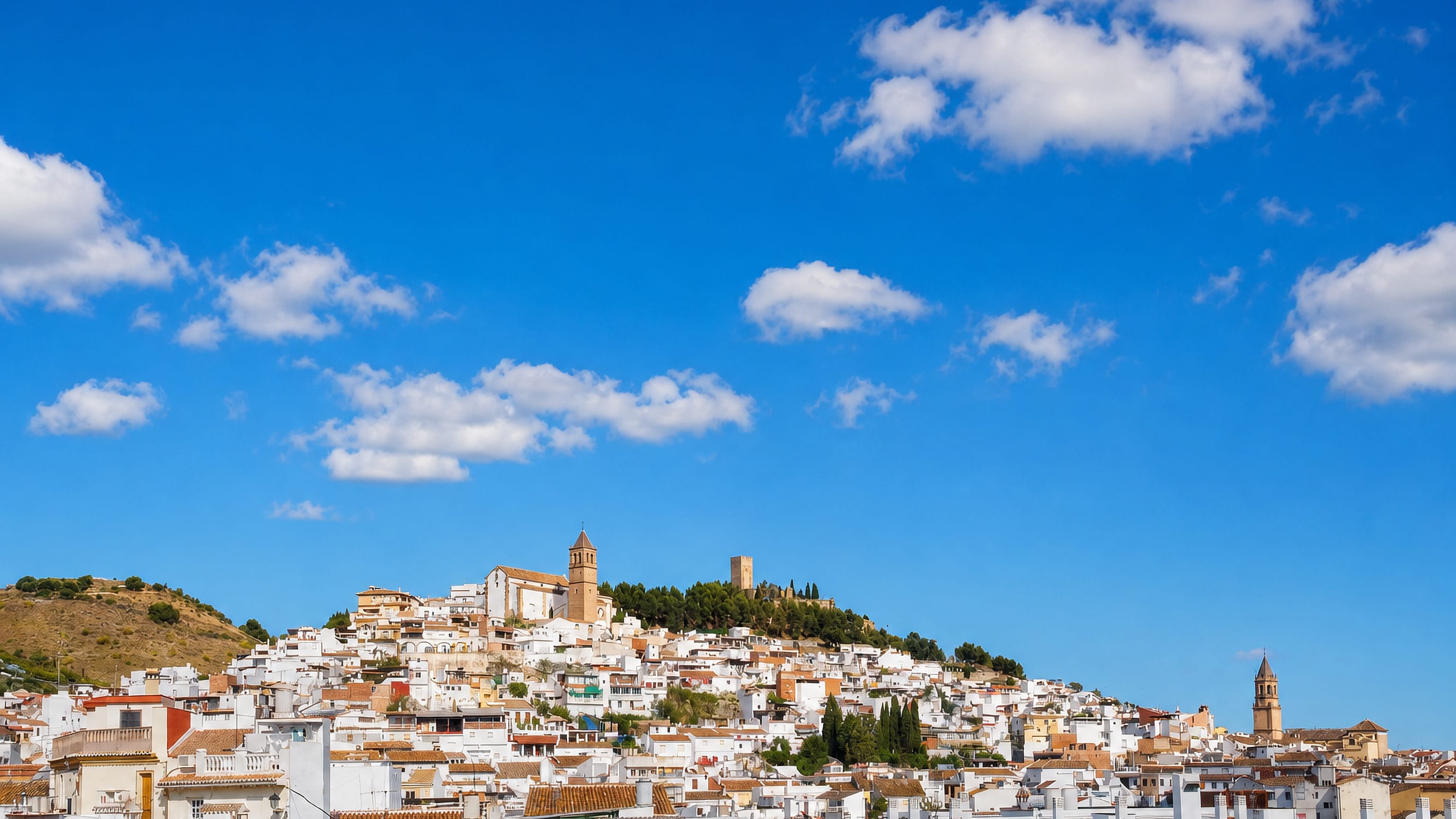Whitewashed houses of Velez-Malaga climbing to its hilltop castle keep and church tower under a blue sky
