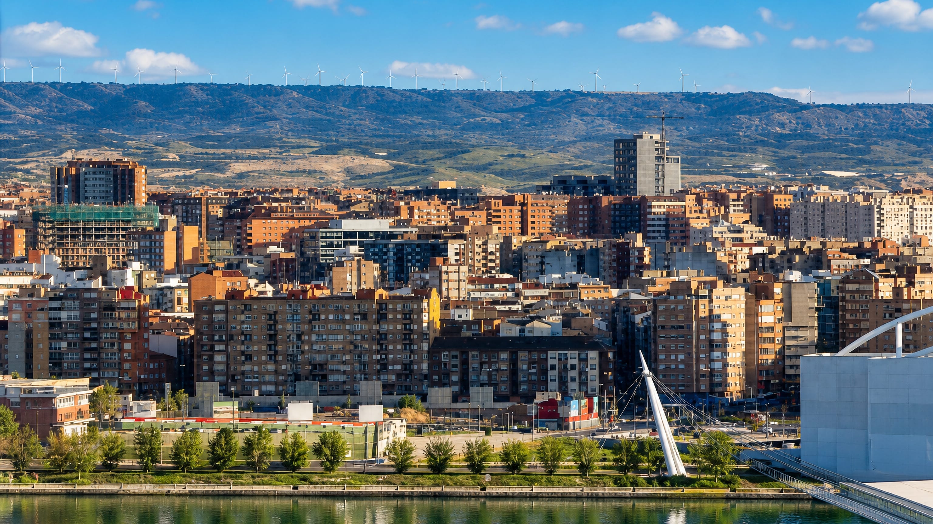 Dense brick apartment blocks of the Delicias district in Zaragoza beside the Ebro, with wind-farm hills behind