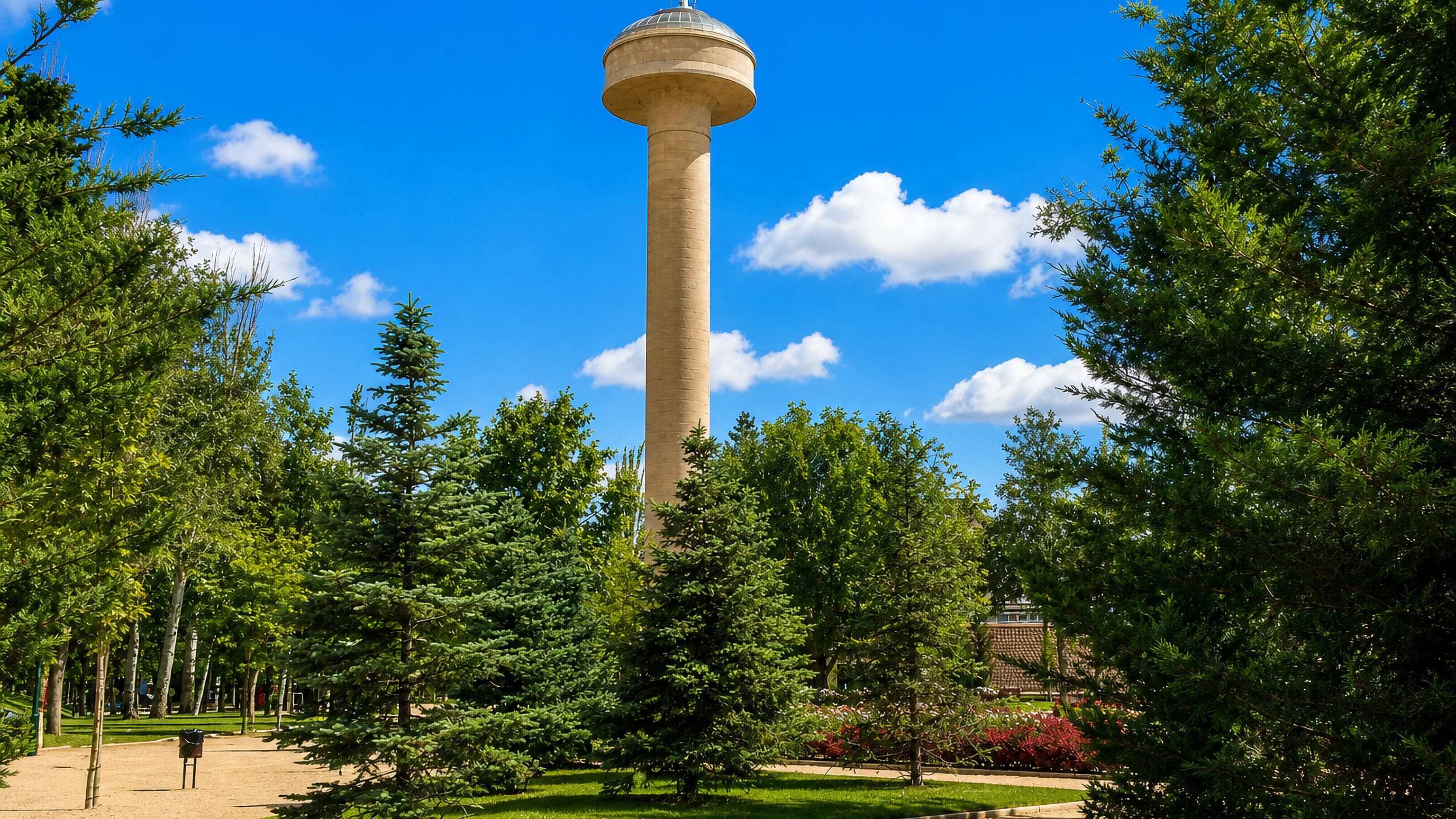 Albacete's mushroom-shaped elevated water tower rising above the pines of a city park under blue sky