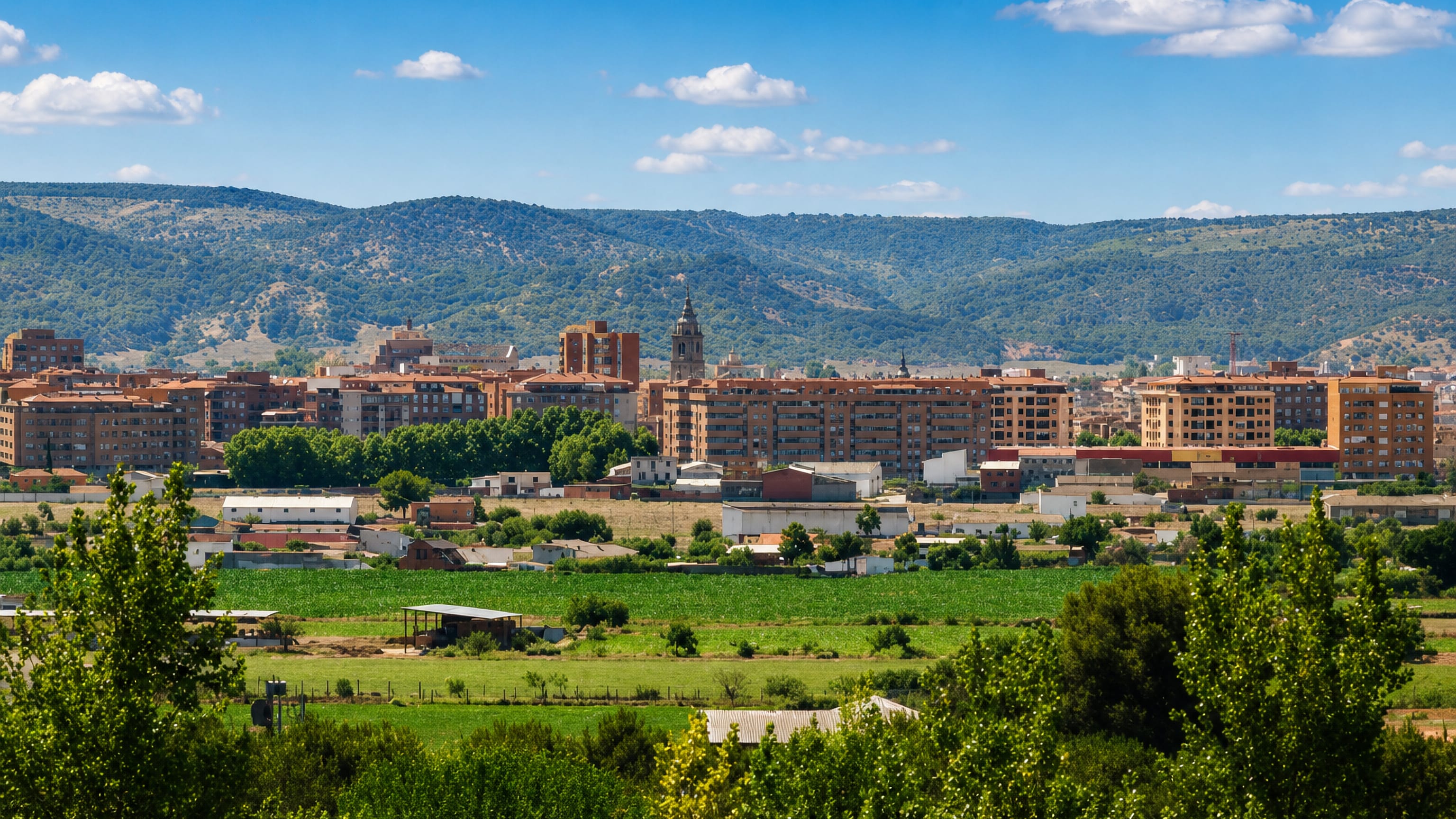 Talavera de la Reina's brick apartment blocks and church tower rise across green farmland below wooded hills.