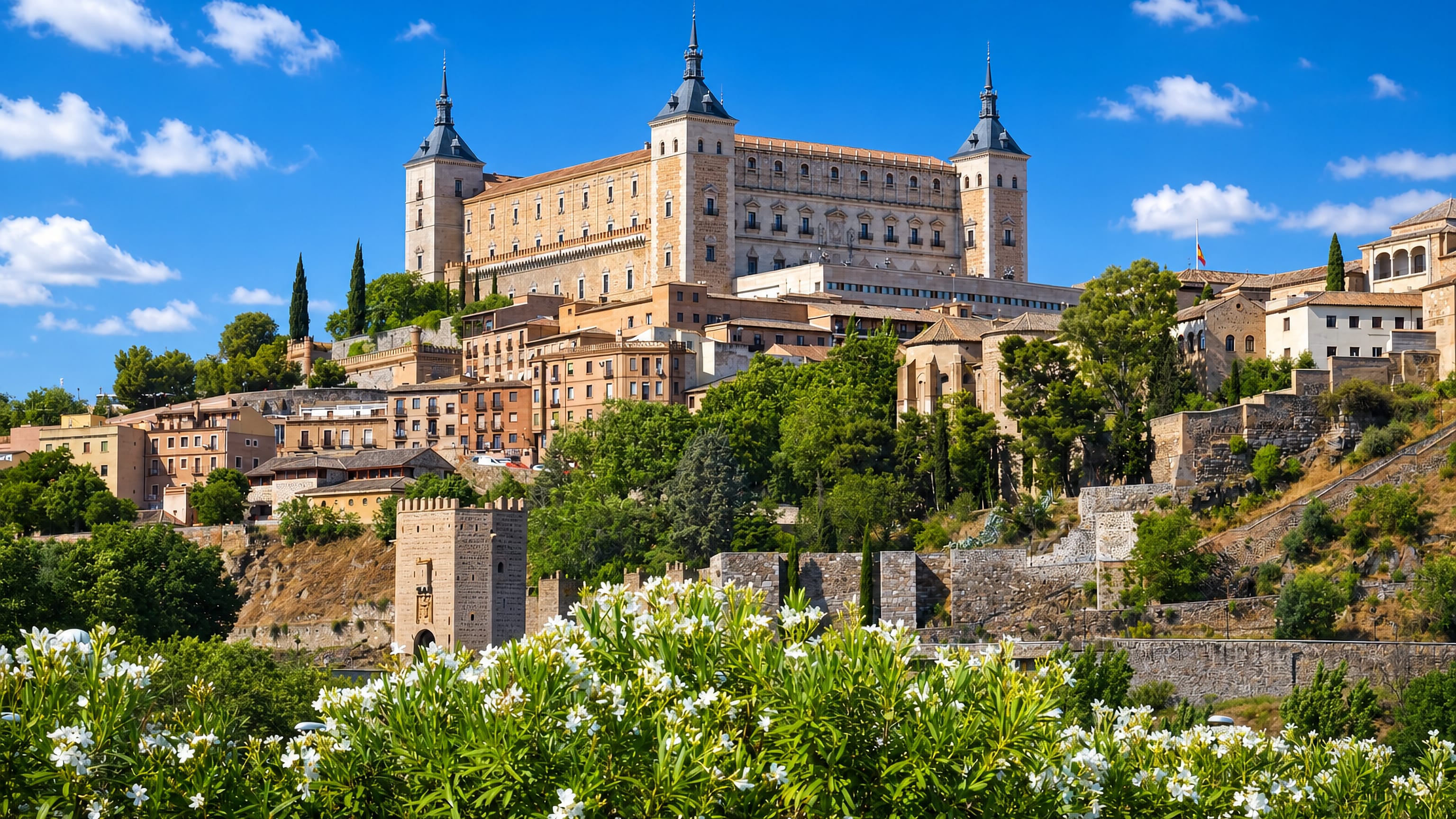 Toledo's Alcazar fortress crowning the old town above the city walls, with oleander in bloom below.