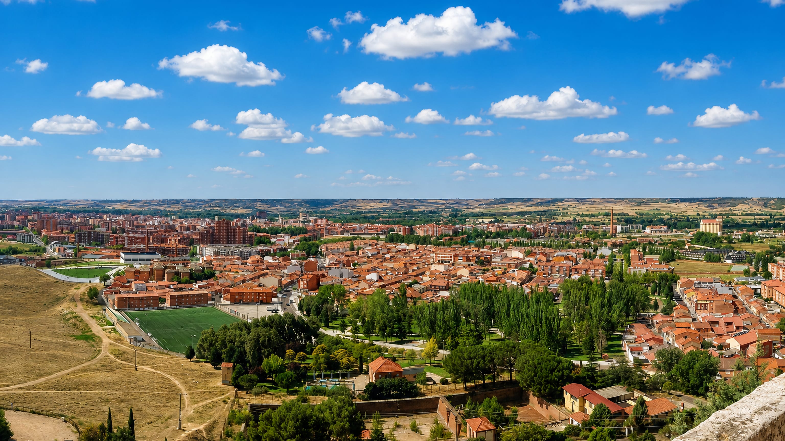 Panoramic view over Palencia's red-tiled rooftops and green parkland with the Castilian plateau beyond.