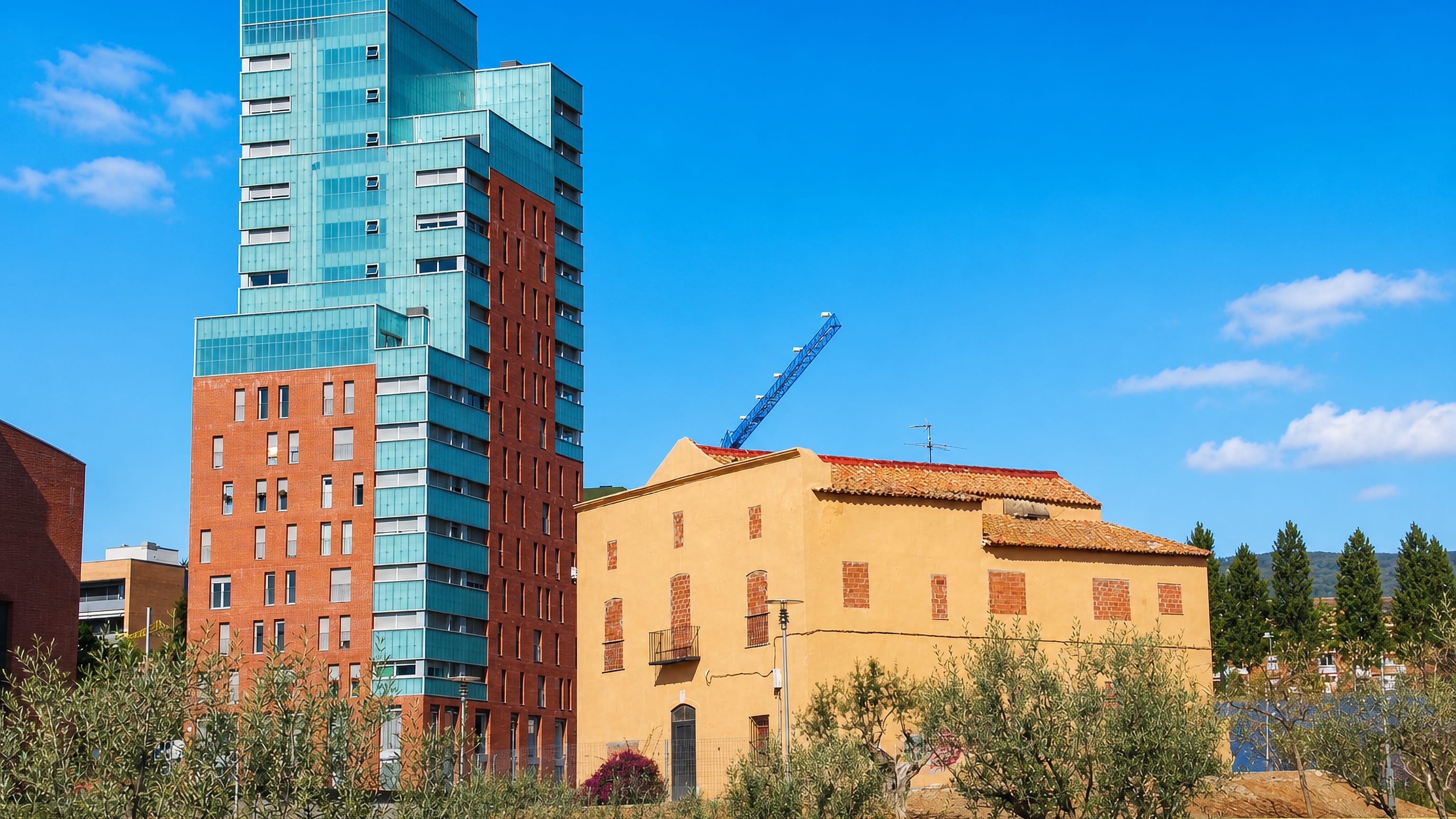Glass-and-brick tower beside an old ochre masia farmhouse in Can Peguera, Barcelona.