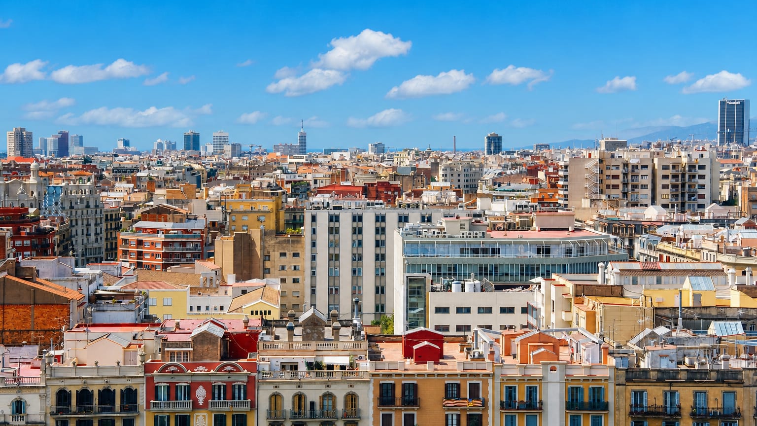 Wide rooftop panorama over Barcelona's Eixample showing ornate apartment facades and a sea of city rooftops