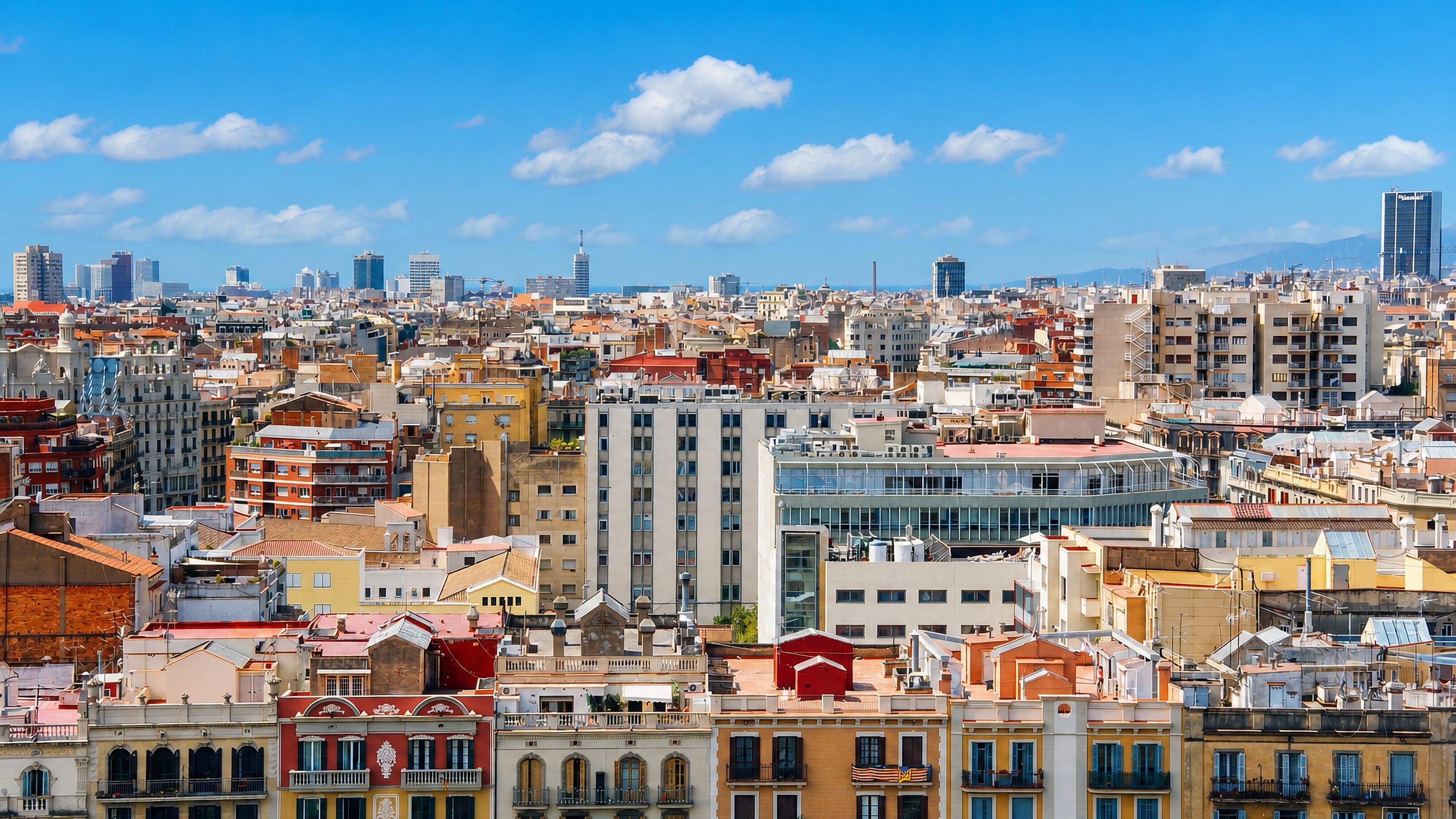 Wide rooftop panorama over Barcelona's Eixample showing ornate apartment facades and a sea of city rooftops