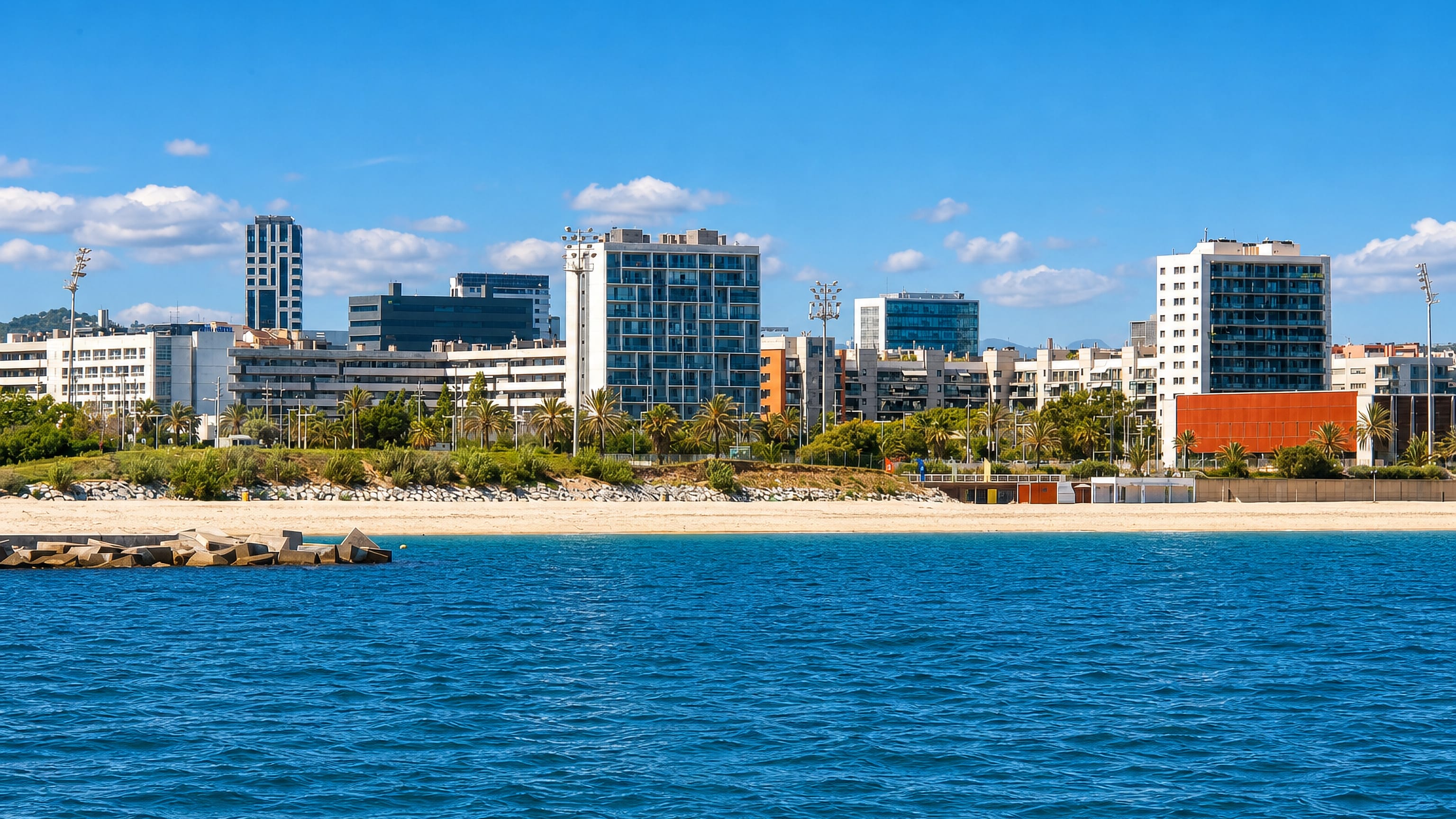 Modern apartment blocks and the palm-lined beachfront of el Poblenou seen across the sea, Barcelona.