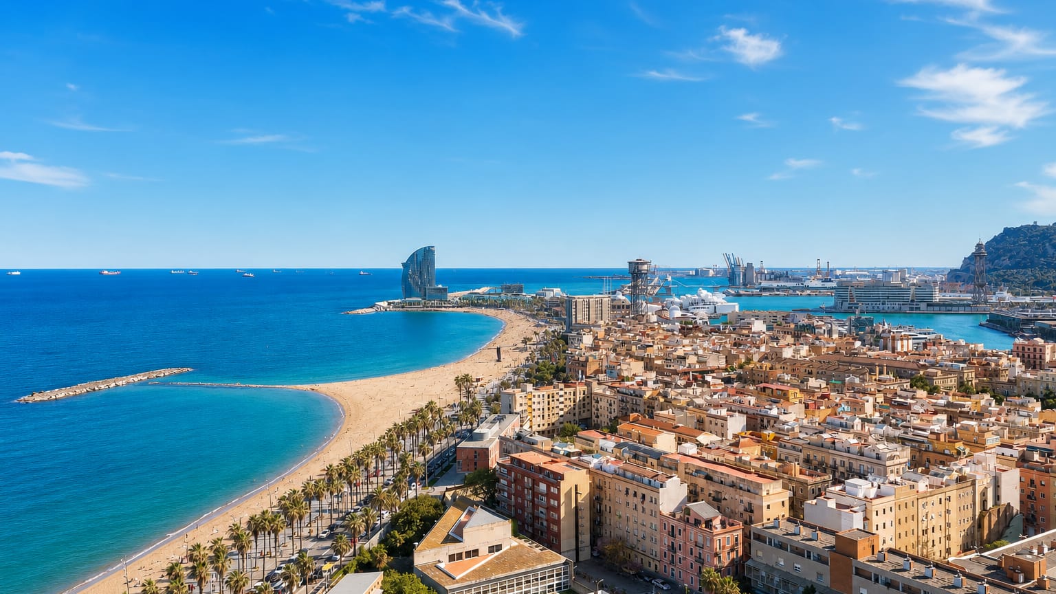 Aerial view of Barcelona's La Barceloneta beach, palm-lined promenade, neighbourhood grid and the sail-shaped W Hotel