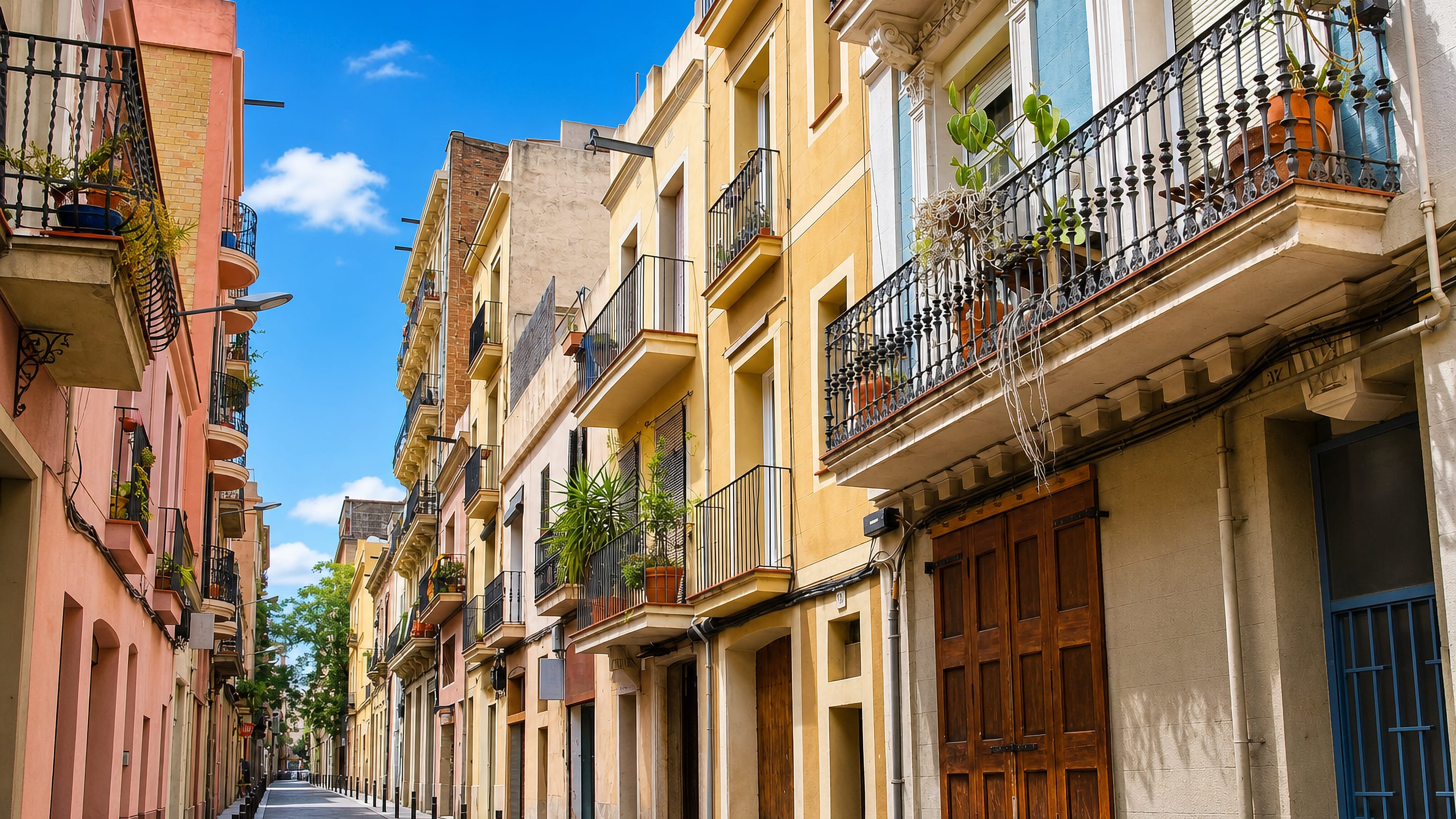 Narrow street of pastel houses with plant-filled wrought-iron balconies in la Vila de Gràcia, Barcelona