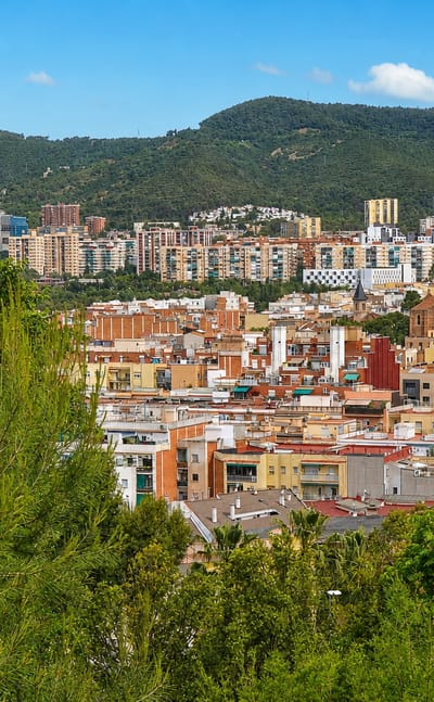 Residential apartment blocks of Nou Barris, Barcelona, framed by trees below the wooded Collserola hills