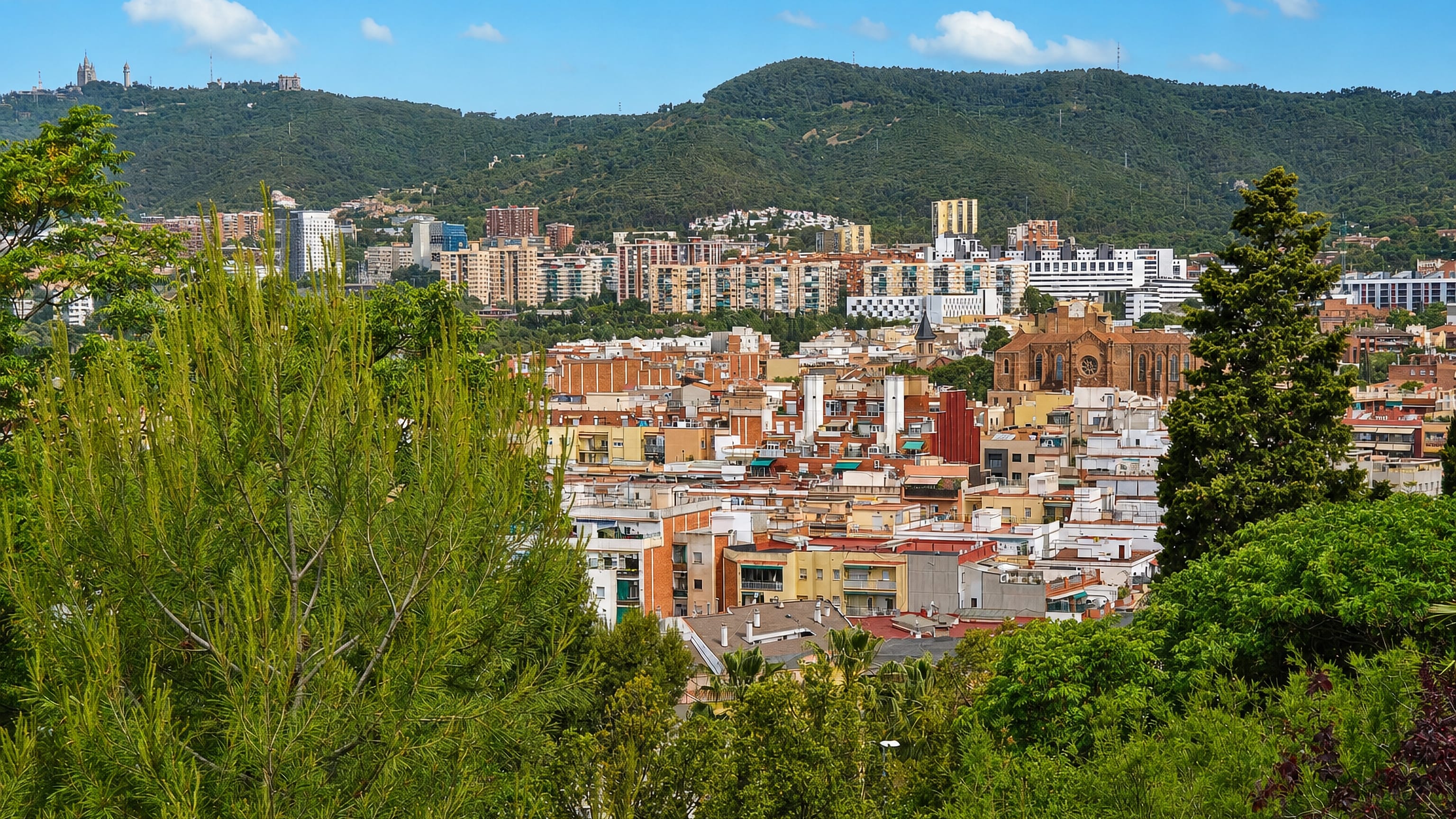 Residential apartment blocks of Nou Barris, Barcelona, framed by trees below the wooded Collserola hills