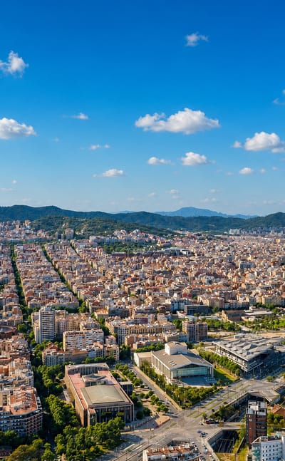 Aerial over Barcelona's Eixample grid with the Sagrada Familia basilica and Torre Glories on the horizon.