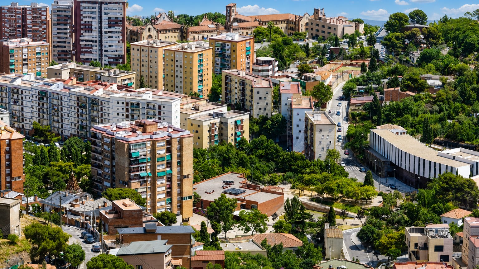 Aerial view over the leafy hillside residential district of Sant Genis dels Agudells in Barcelona, with mid-rise blocks among greenery under a blue sky.