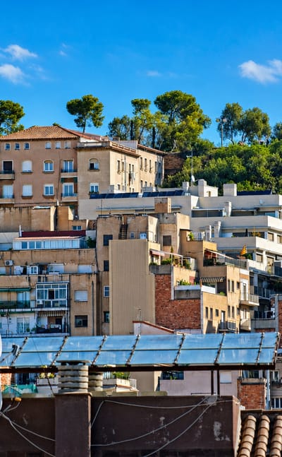 Apartment blocks climbing a wooded hillside crowned by a monument in the Vallcarca neighbourhood of Barcelona.
