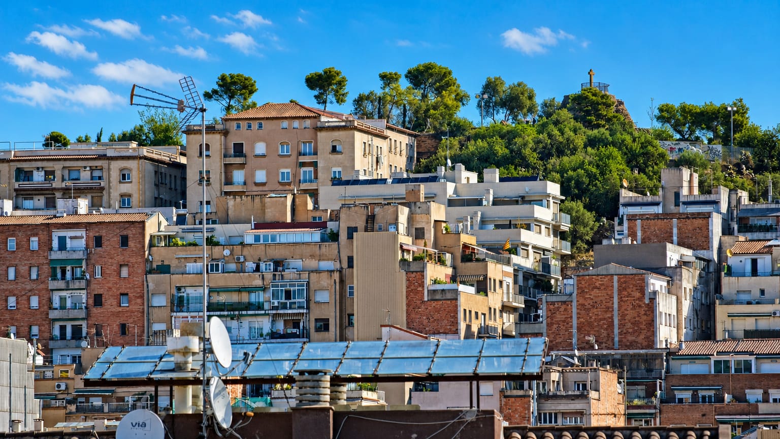 Apartment blocks climbing a wooded hillside crowned by a monument in the Vallcarca neighbourhood of Barcelona.