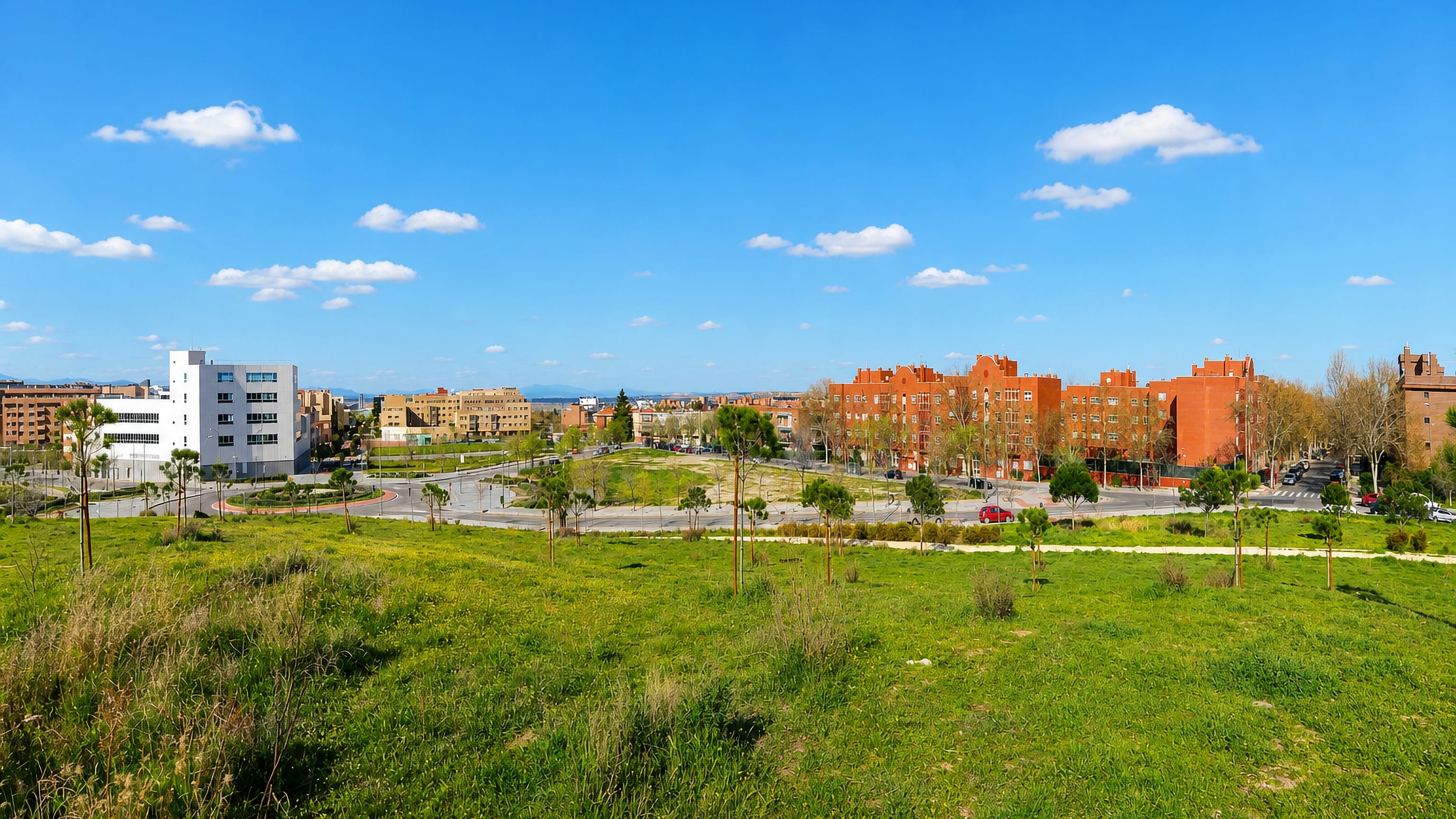 Red-brick apartment blocks and offices across open green parkland in the Timon area of Alcobendas, Madrid.