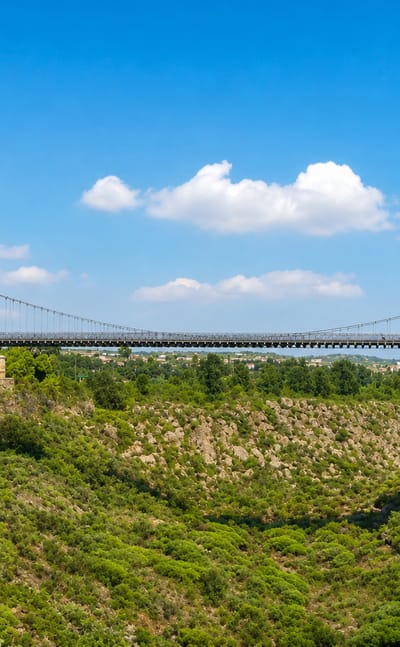 Historic suspension bridge spanning a green valley under a bright blue sky at Amposta on the Ebro