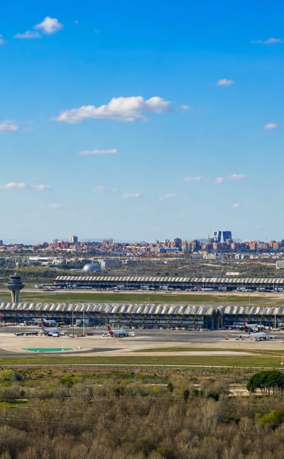 Madrid-Barajas Airport Terminal 4's wavy roof and control tower with the Cuatro Torres skyline behind, in the Barajas district