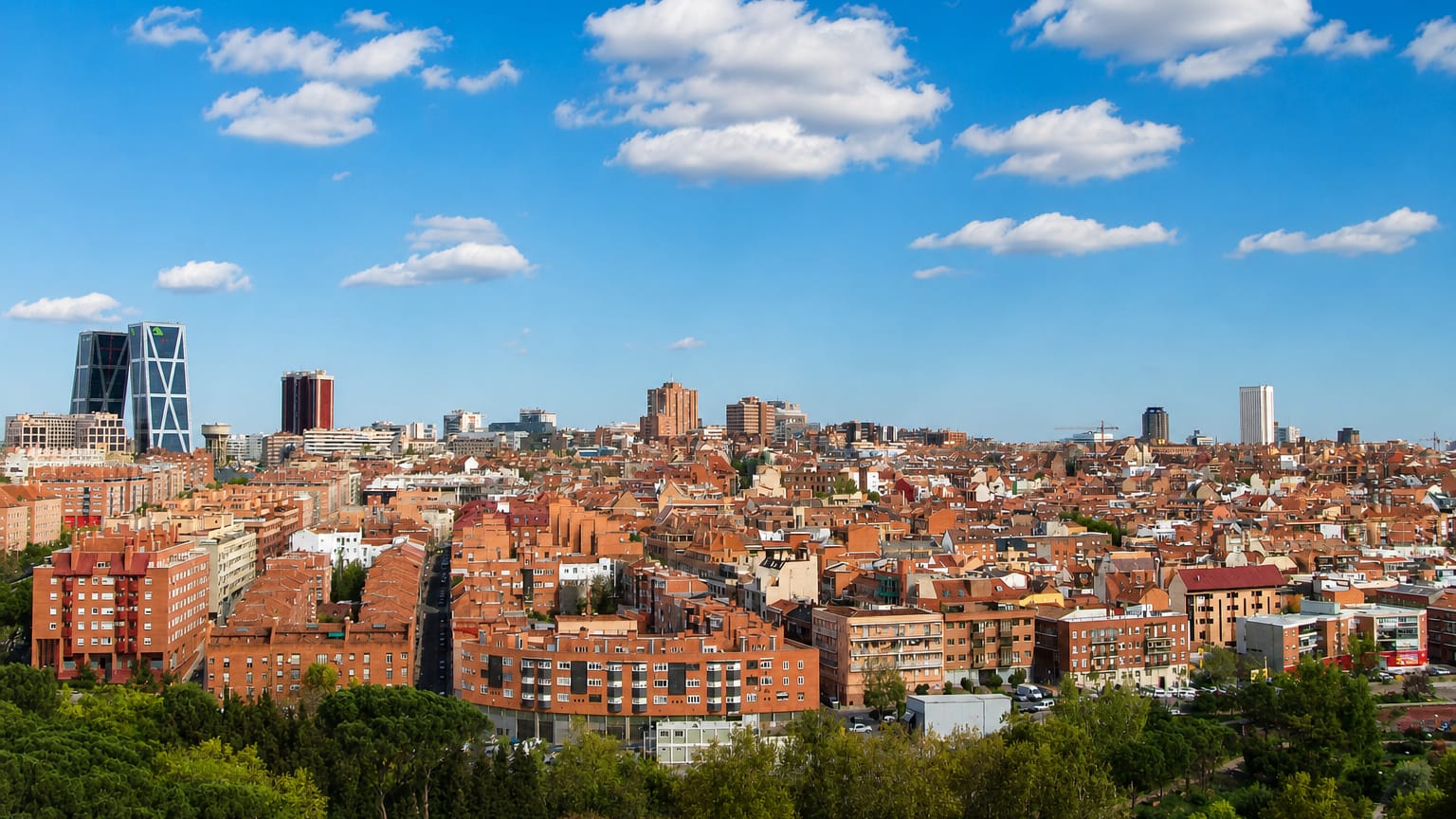 Wide daytime Madrid rooftop skyline with the Cuatro Torres and KIO towers on the horizon