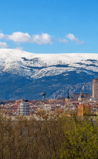 Central Madrid skyline with the Torre de Madrid and Faro de Moncloa against the snow-capped Sierra de Guadarrama.