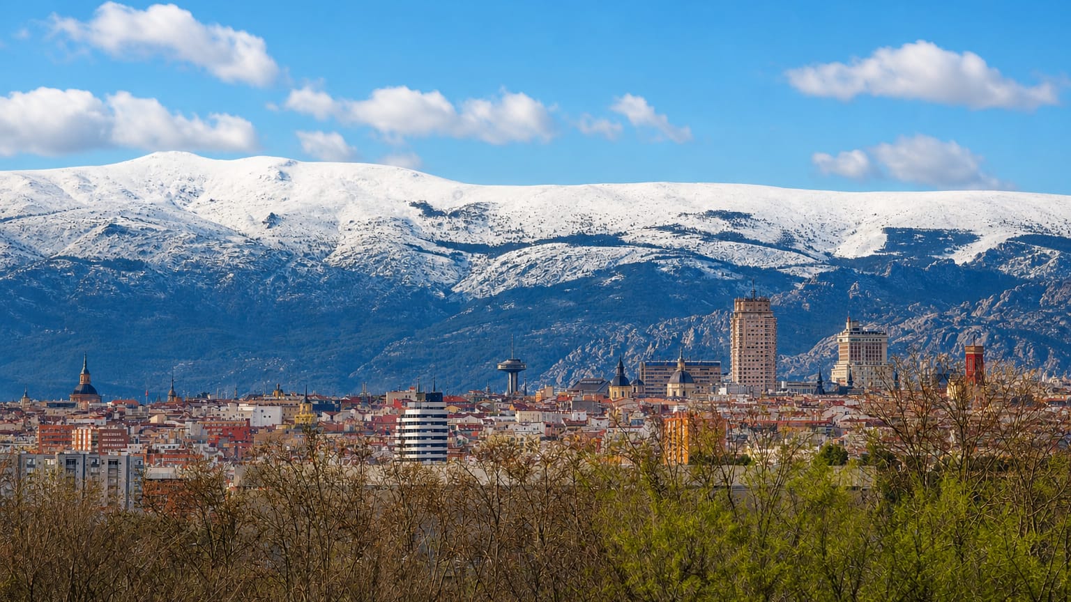 Central Madrid skyline with the Torre de Madrid and Faro de Moncloa against the snow-capped Sierra de Guadarrama.