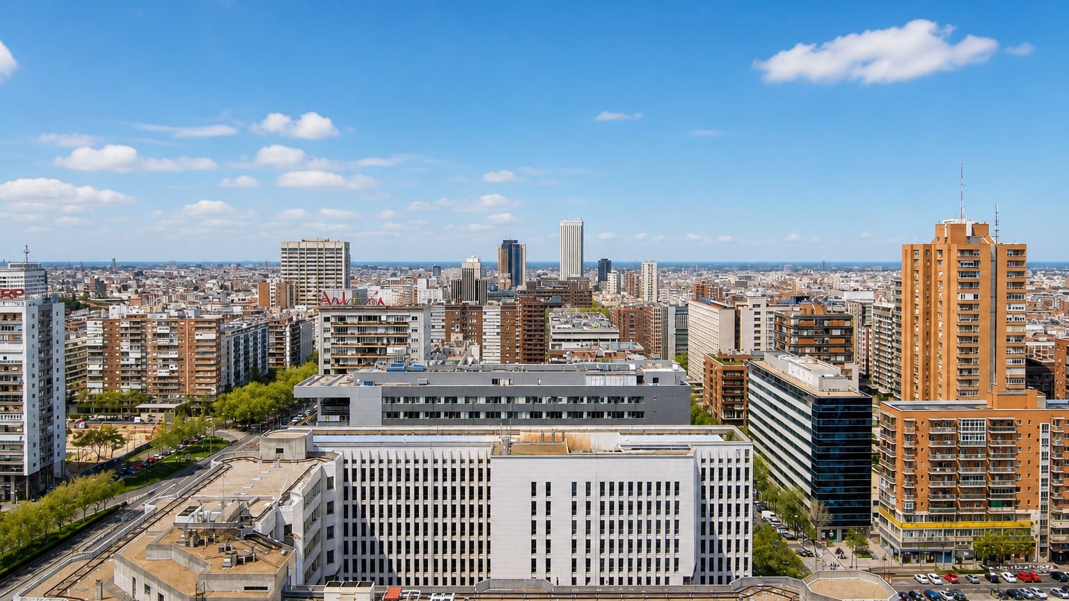 Aerial daytime view of Madrid's Castillejos district, dense apartment blocks with the Cuatro Torres faint on the horizon.