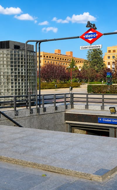 Metro station entrance signed Ciudad Universitaria before university campus buildings in Madrid