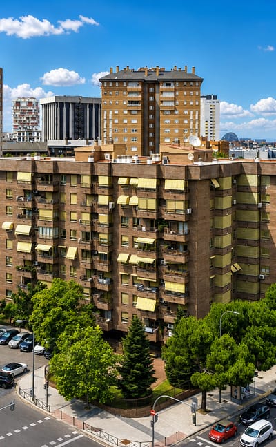 Daytime view of Madrid's Costillares district with residential tower blocks, tree-lined streets and a swimming pool.