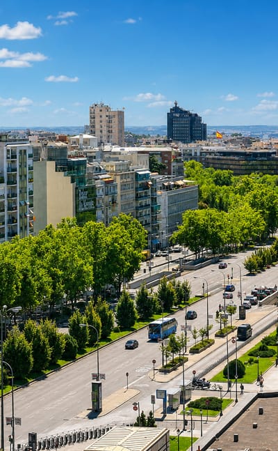 Leafy tree-lined boulevard and mid-rise residential blocks with the Madrid skyline in the El Viso district.