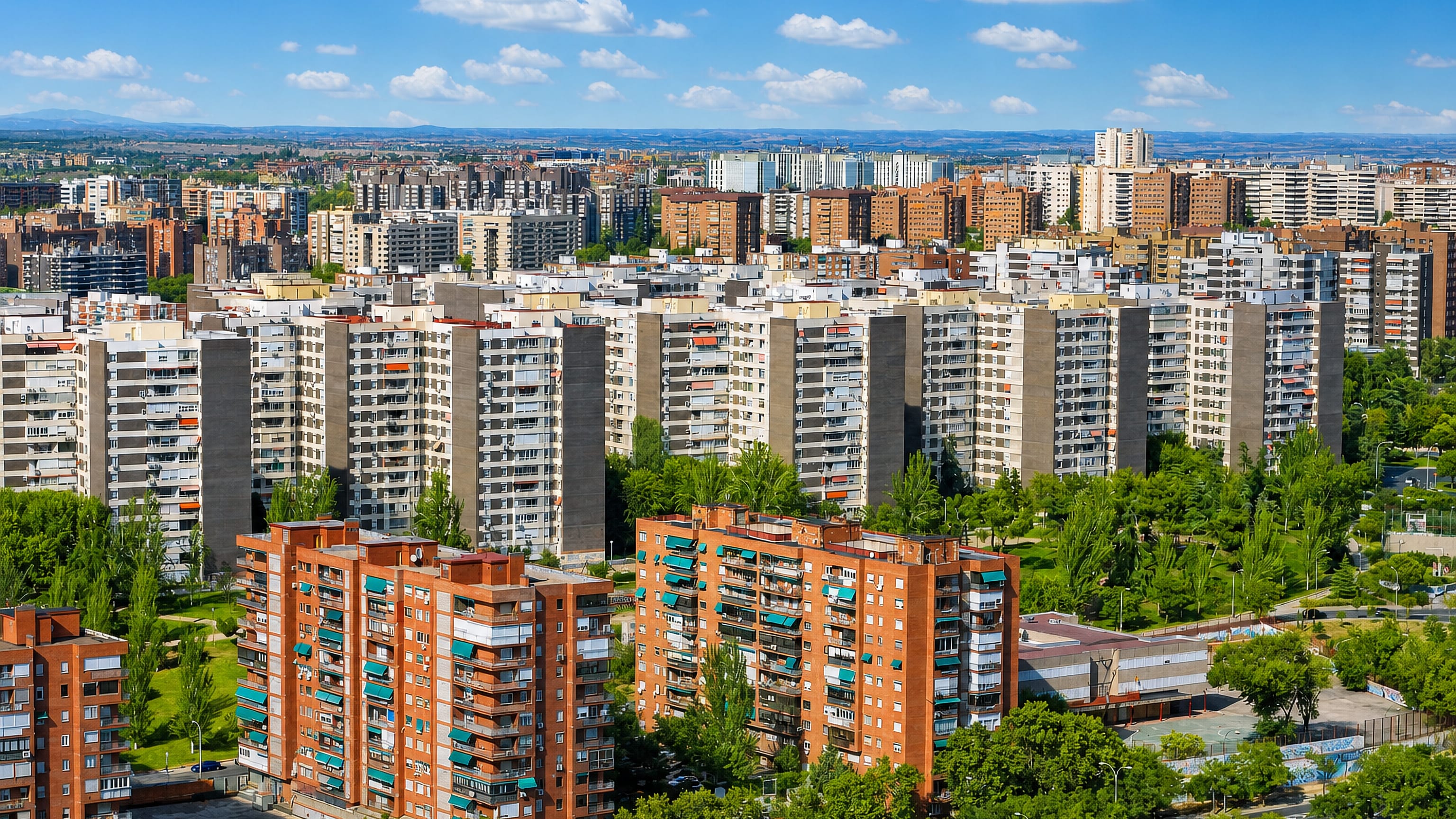 Aerial view over Fuencarral, Madrid, with high-rise apartment blocks, leafy streets and the sierra beyond.