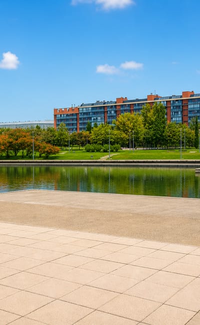 Modern lakeside park with a paved plaza and red-brick apartment block in Madrid.