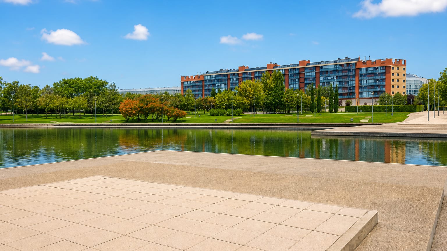 Modern lakeside park with a paved plaza and red-brick apartment block in Madrid.