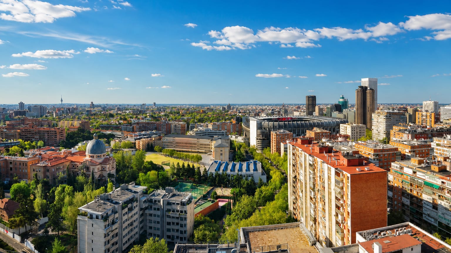 Aerial view over a dense Madrid residential district with green courtyards and the Cuatro Torres in the distance