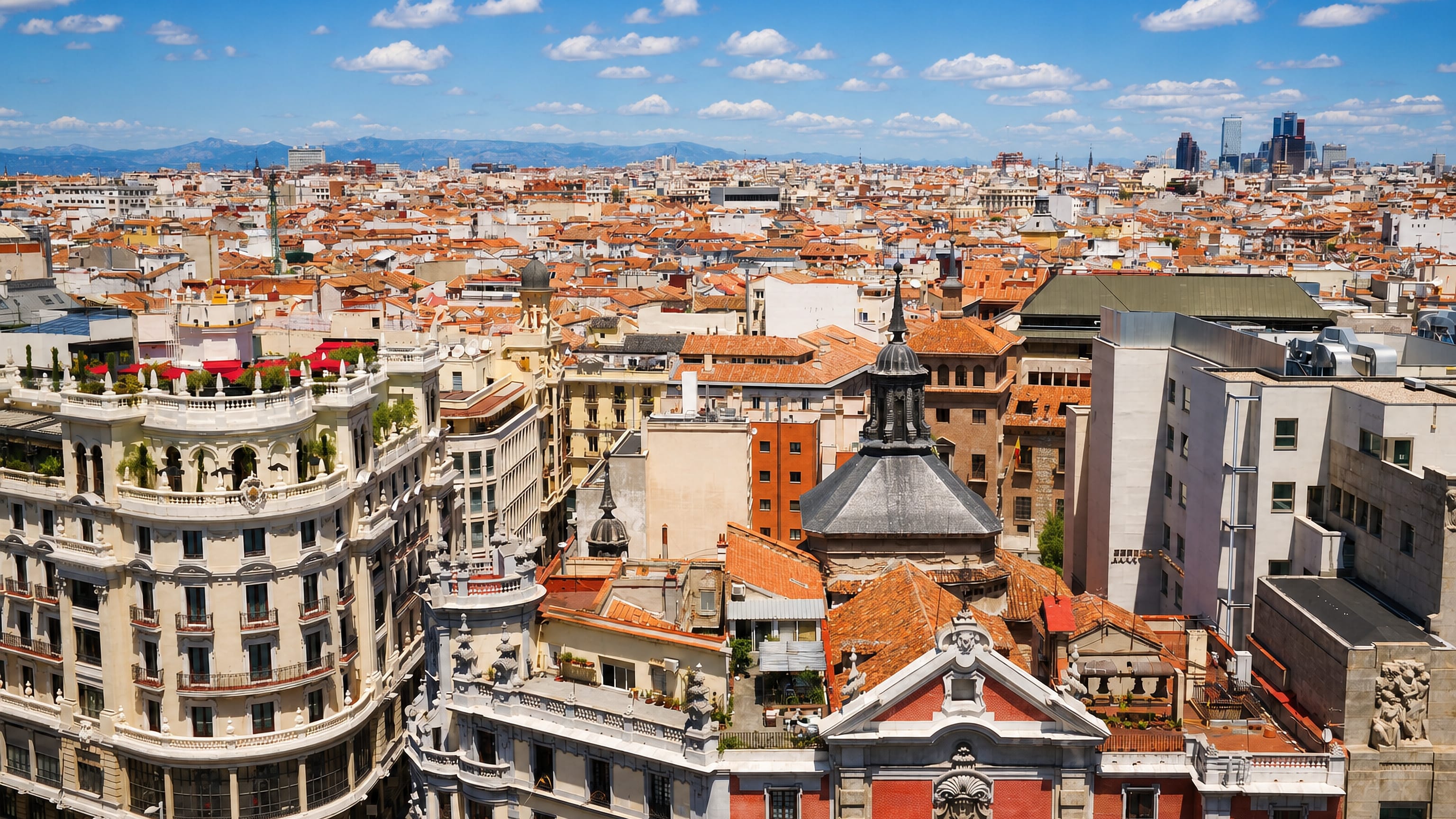 Terracotta rooftops and domes of Madrid's Justicia district, with the Cuatro Torres on the far skyline.