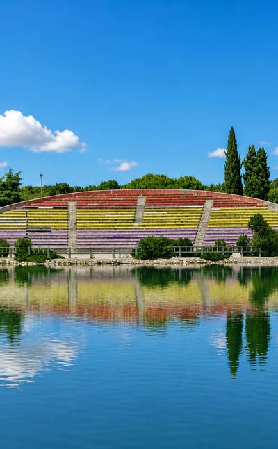 Colourful tiered park amphitheatre mirrored in a lake amid green trees in Las Aguilas, Madrid